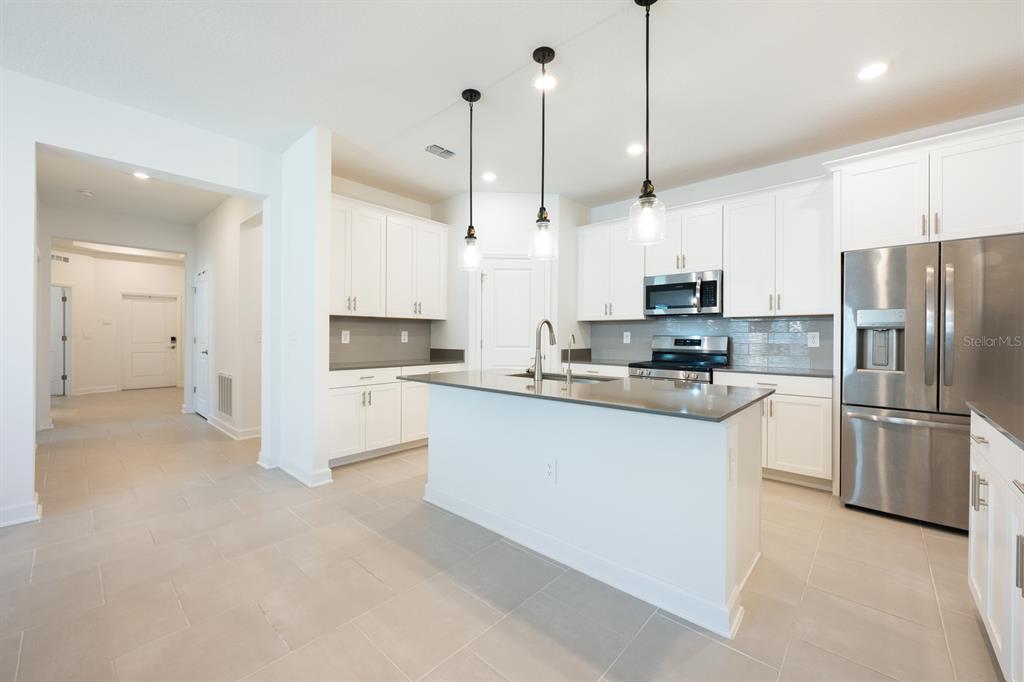 A modern kitchen features white cabinets, stainless steel appliances, a center island, and tile flooring — 1874 FLOURISH AVENUE, KISSIMMEE, FL