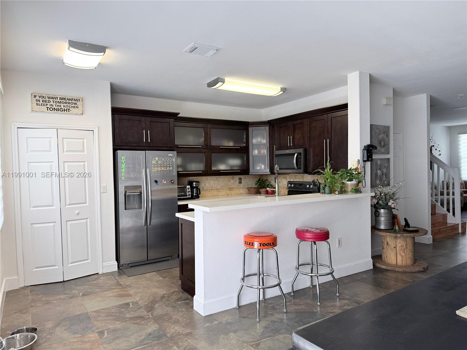 A kitchen features dark wood cabinets, stainless steel appliances, a breakfast bar, and tile flooring — 7809 NW 114th Path, Doral FL 33178, DORAL, FL