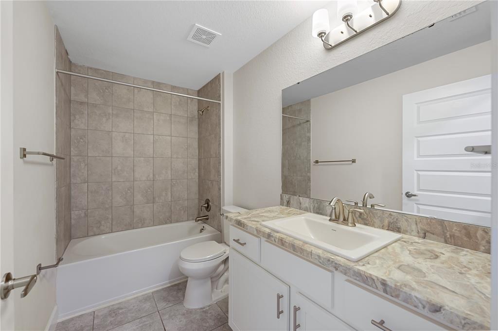 A bathroom features a tiled tub-shower combo, a white vanity with stone countertop, and mirror — 430 PANARO LANE, HAINES CITY, FL