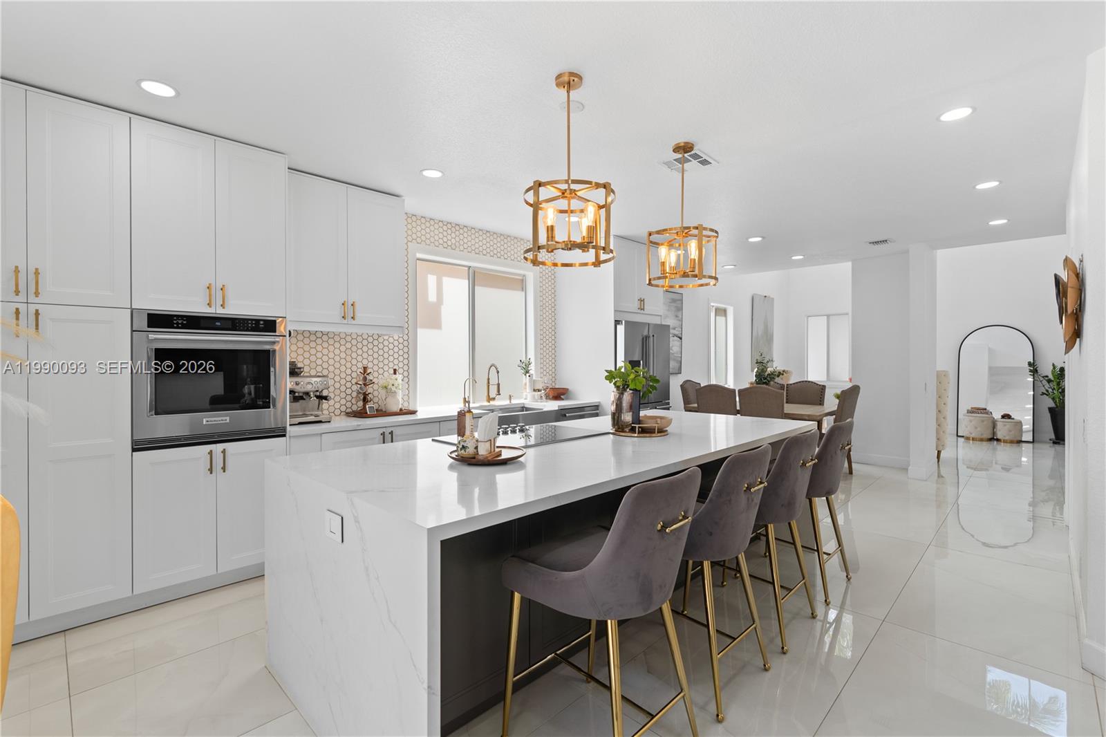 A modern kitchen features white cabinetry, a marble-topped island, and gold pendant lighting — 1500 Canary Island Dr, Weston FL 33327, WESTON, FL