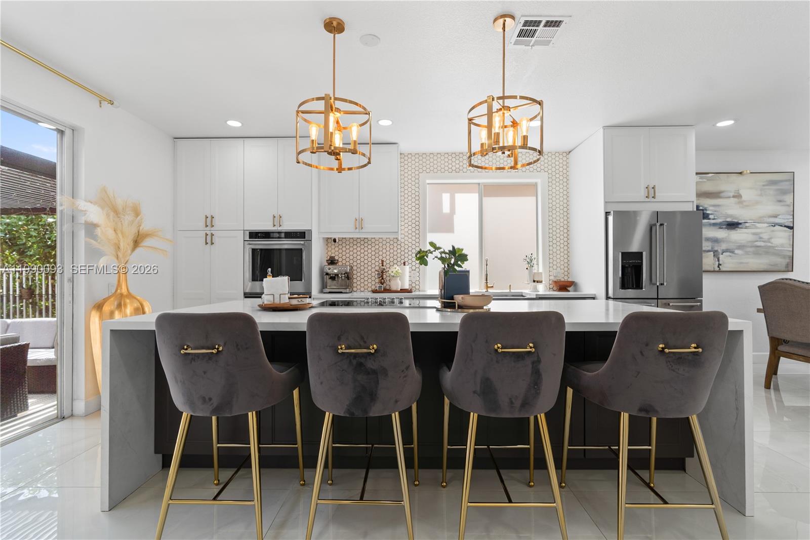 A modern kitchen features a large island with four gray velvet barstools and gold accents — 1500 Canary Island Dr, Weston FL 33327, WESTON, FL
