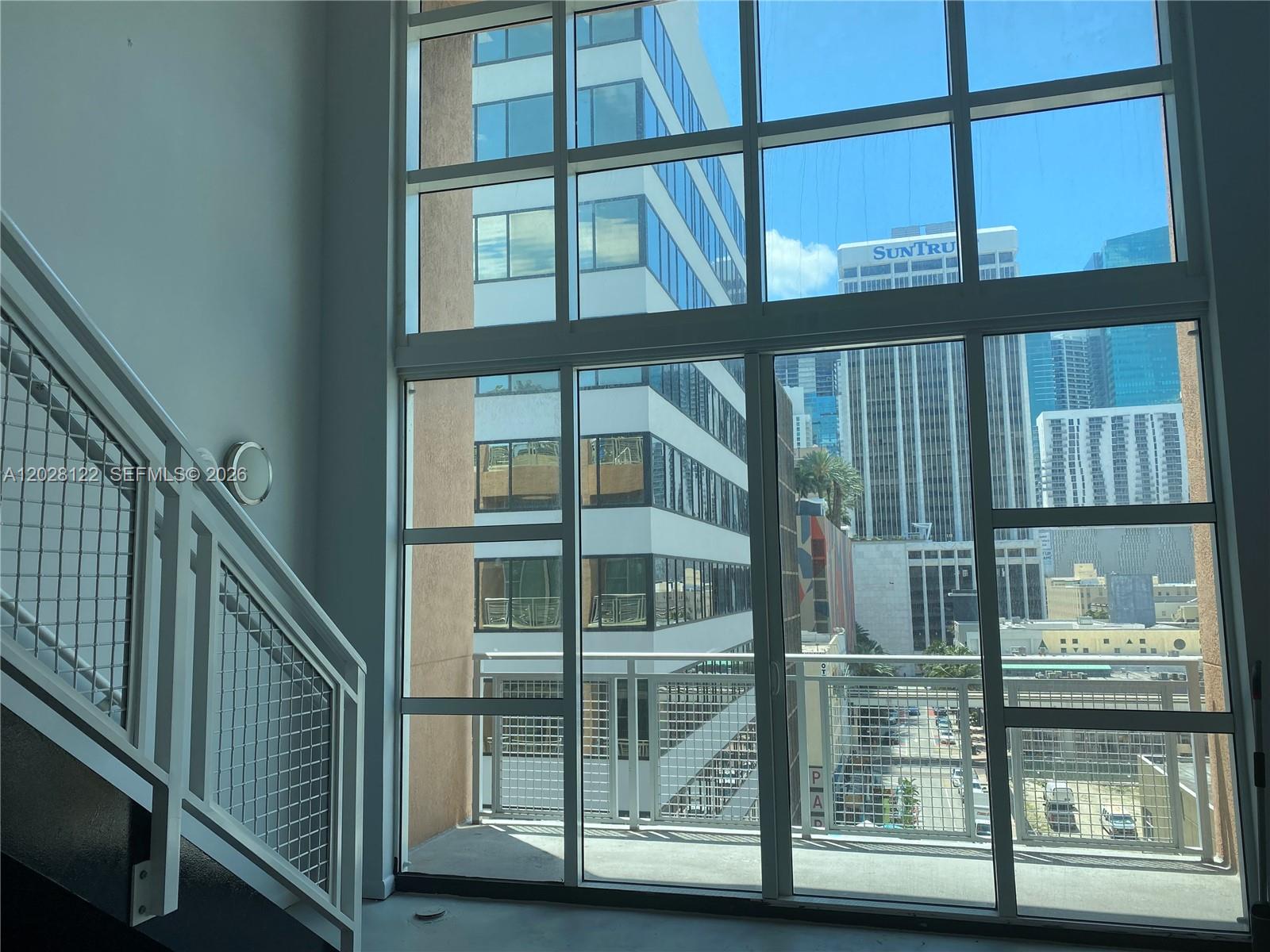 A room with a staircase and floor-to-ceiling windows overlooking a city skyline — 253 NE 2nd St # 621, Miami FL 33132, MIAMI, FL