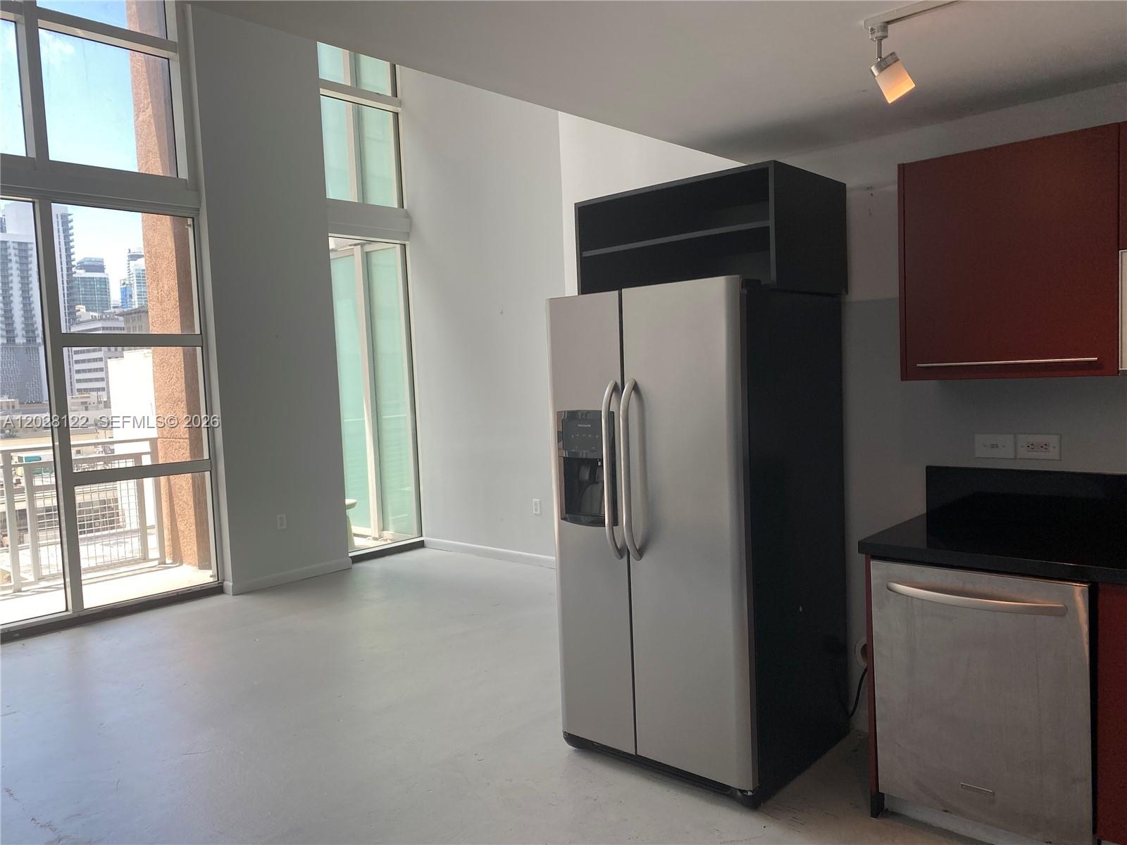 A modern kitchen area features a stainless steel refrigerator and dark cabinets near floor-to-ceiling windows — 253 NE 2nd St # 621, Miami FL 33132, MIAMI, FL