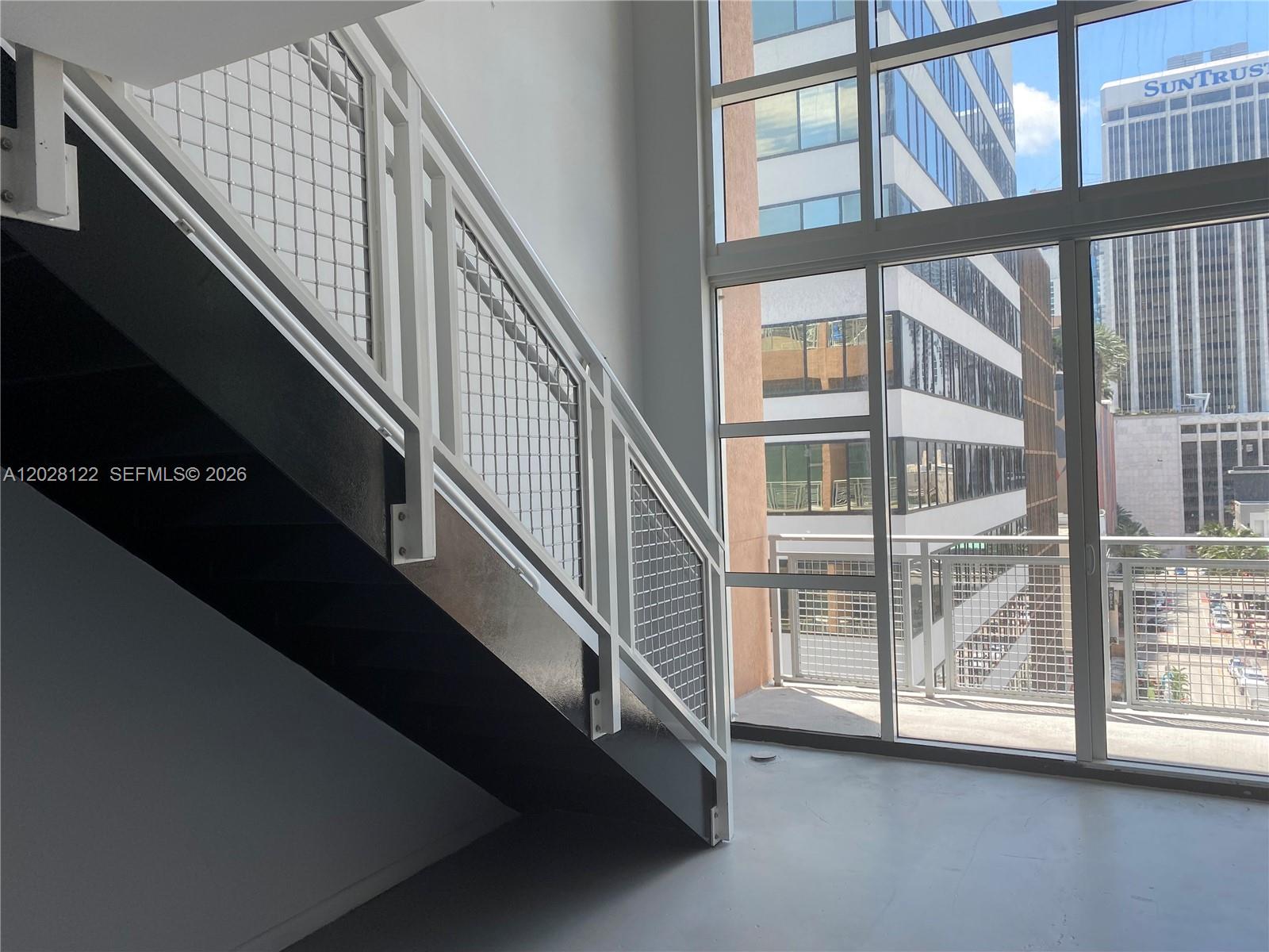A staircase with white metal railings sits next to floor-to-ceiling windows overlooking city buildings — 253 NE 2nd St # 621, Miami FL 33132, MIAMI, FL