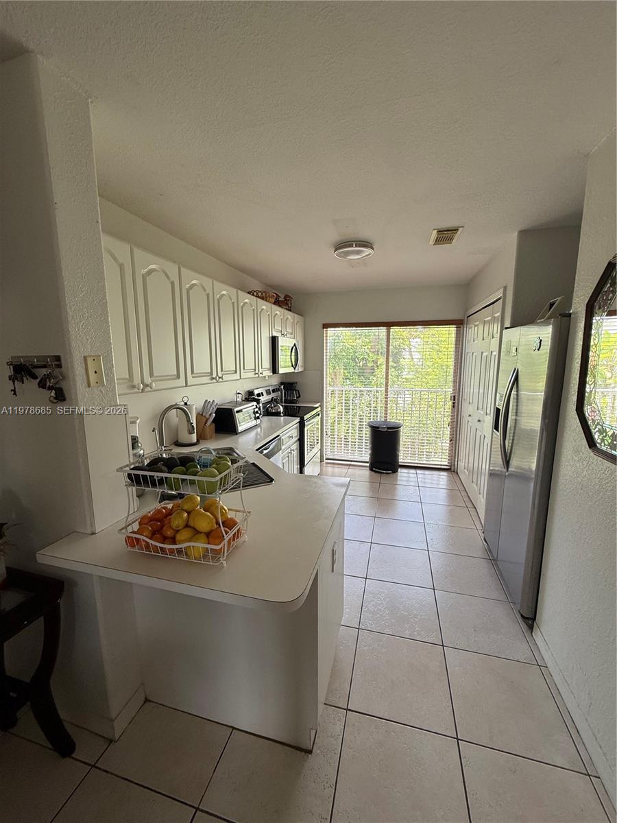 A kitchen features white cabinets, stainless steel appliances, tile flooring, and a sliding glass door — 5605 NW 109th Ave # 76, Doral FL 33178, DORAL, FL