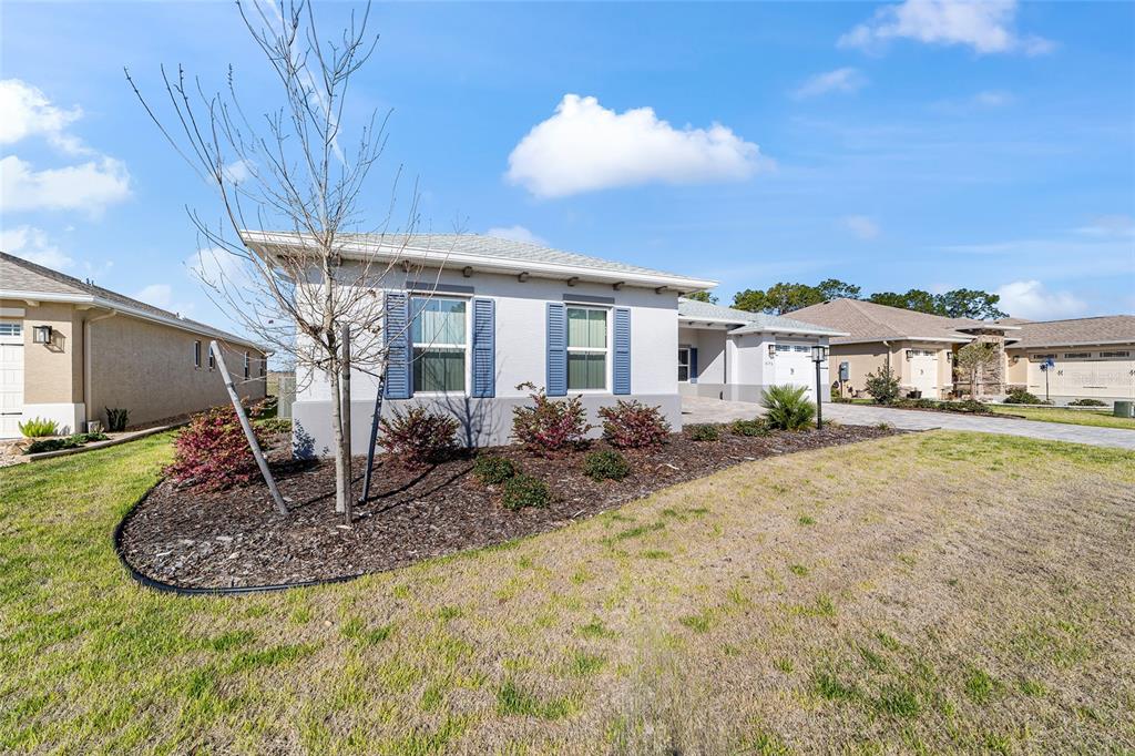 A single-story house with a light-colored stucco exterior, blue shutters, and a landscaped front yard — 8176 SW 98TH TERRACE ROAD, OCALA, FL