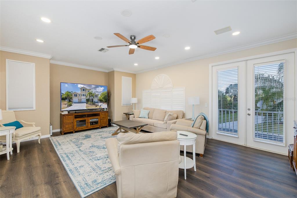 A living room features a large television, beige sofa, armchairs, and glass doors to a patio — 3020 SHEPPARDS CROOK COURT, HOLIDAY, FL