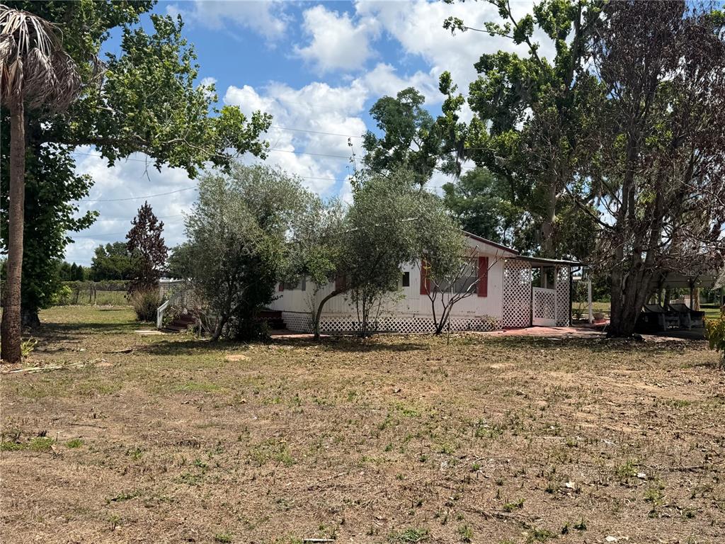 A single-story mobile home with white siding sits on a large, grassy lot — 10006 CAUSEY PL, THONOTOSASSA, FL