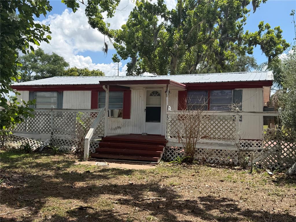 A single-story mobile home with a metal roof, red trim, and a lattice-enclosed front deck — 10006 CAUSEY PL, THONOTOSASSA, FL