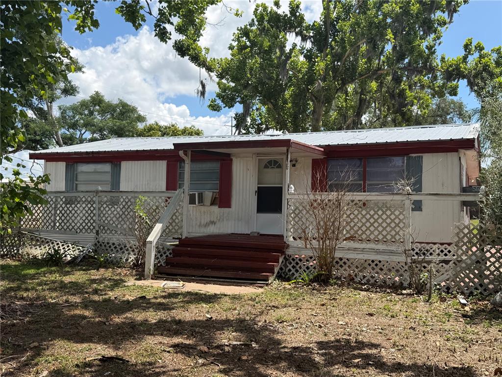 A single-story mobile home features a metal roof, white siding, and a wooden front deck — 10006 CAUSEY PL, THONOTOSASSA, FL