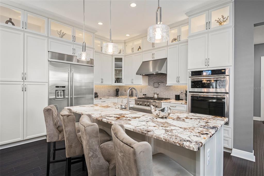 A kitchen features white cabinetry, a large stone island with seating, and stainless steel appliances — 8801 FOUNTAIN PALM ALLEY, WINTER GARDEN, FL