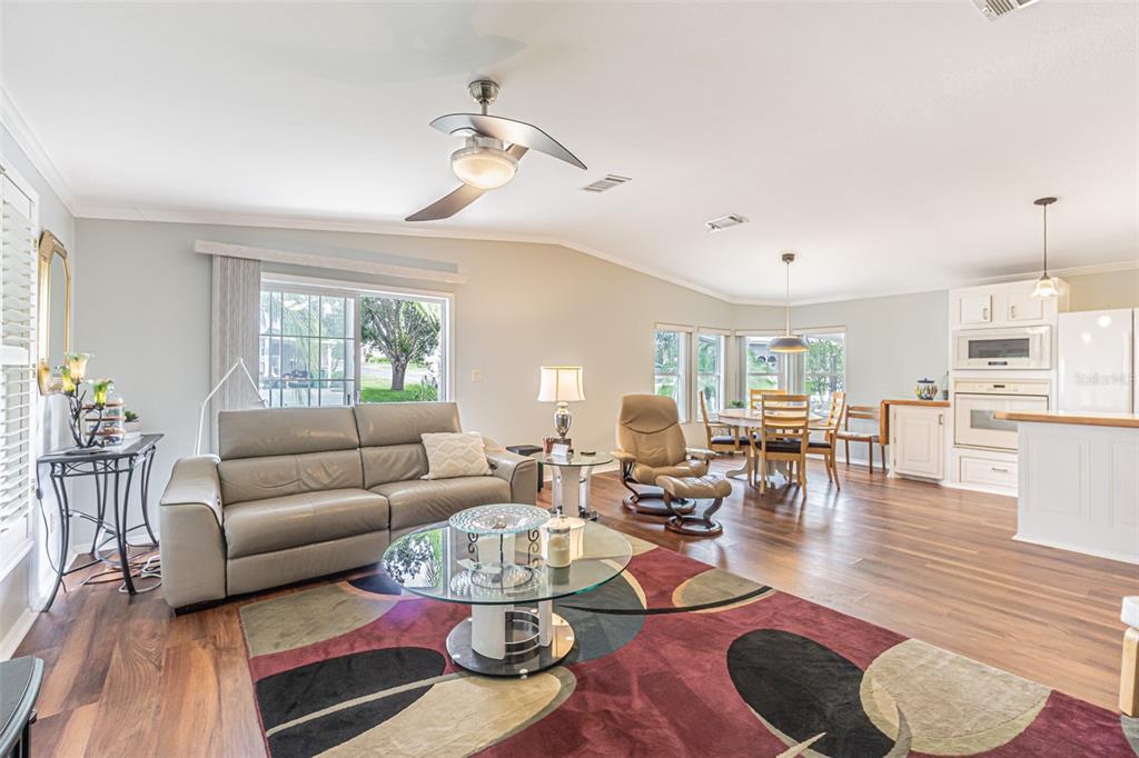 An open-concept living and dining area features wood flooring, a ceiling fan, and white cabinetry — 37654 NEUKOM AVENUE, ZEPHYRHILLS, FL