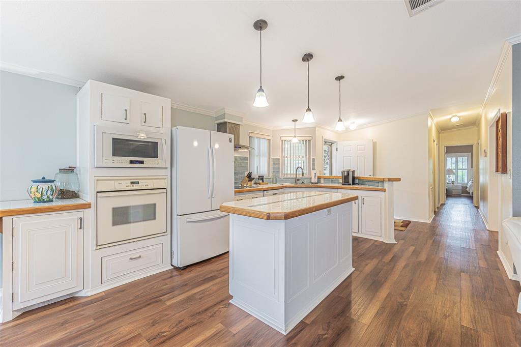 A kitchen features white cabinets, a central island, stainless appliances, and wood-look flooring — 37654 NEUKOM AVENUE, ZEPHYRHILLS, FL