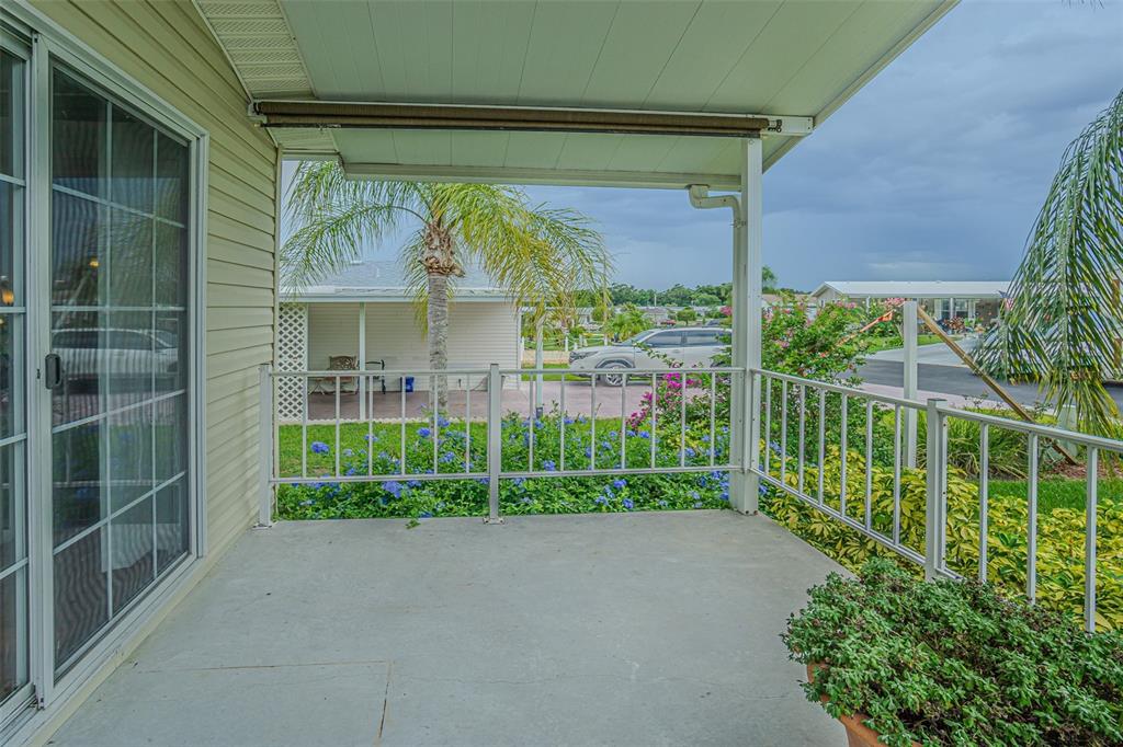 A covered concrete patio with white railings overlooks a landscaped yard and neighboring homes — 37654 NEUKOM AVENUE, ZEPHYRHILLS, FL