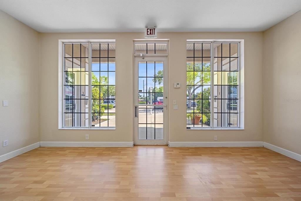 A room with light-colored walls, wood-look flooring, two large windows, and a central glass door — 3900 CLARK ROAD UNIT D2, SARASOTA, FL