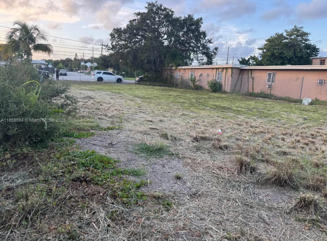 A vacant, grassy lot sits adjacent to a single-story peach-colored building and a chain-link fence — 1950 Ali Baba Ave, Opa-Locka FL 33054, OPA-LOCKA, FL