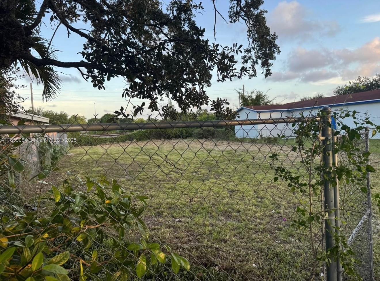 A fenced, grassy vacant lot sits beneath the branches of a large tree — 1950 Ali Baba Ave, Opa-Locka FL 33054, OPA-LOCKA, FL