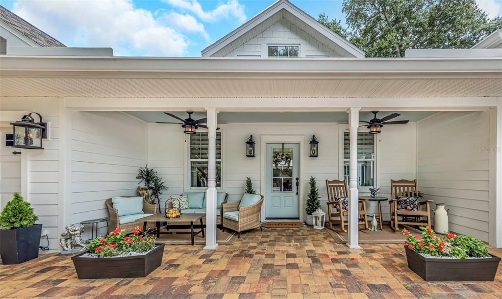 A paved patio features a covered seating area, outdoor furniture, and white exterior siding — 411 ROEBLING ROAD S, BELLEAIR, FL