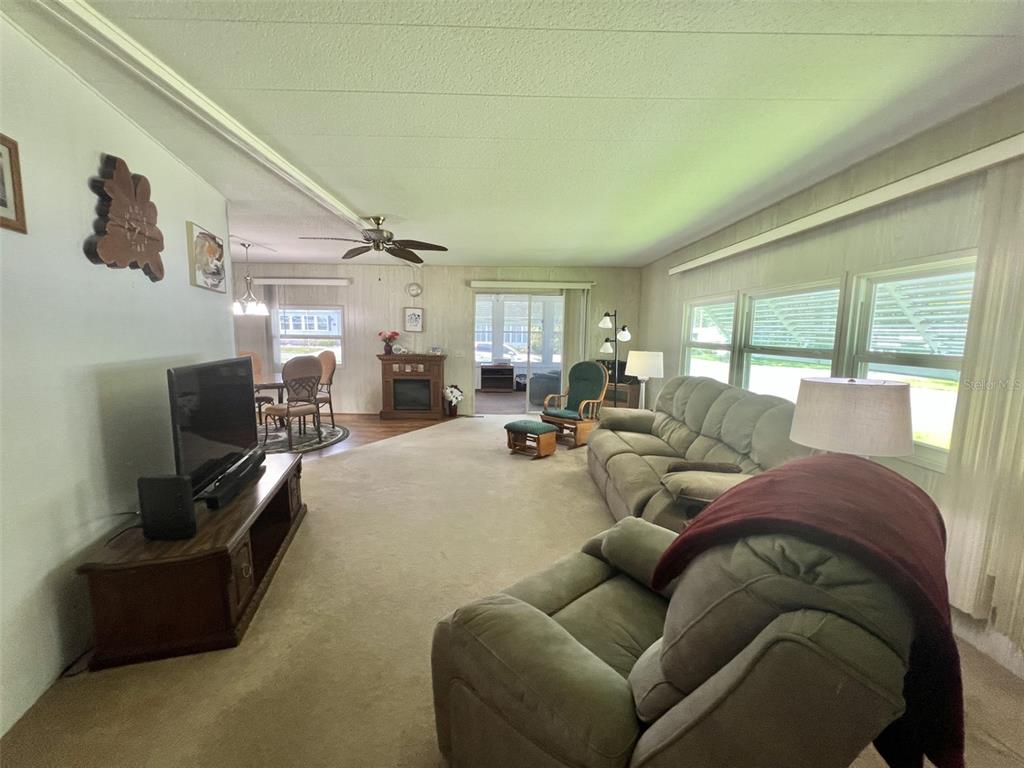 A living room features beige carpeting, a large sectional sofa, a television, and a fireplace — 424 HAWTHORNE BOULEVARD, LEESBURG, FL