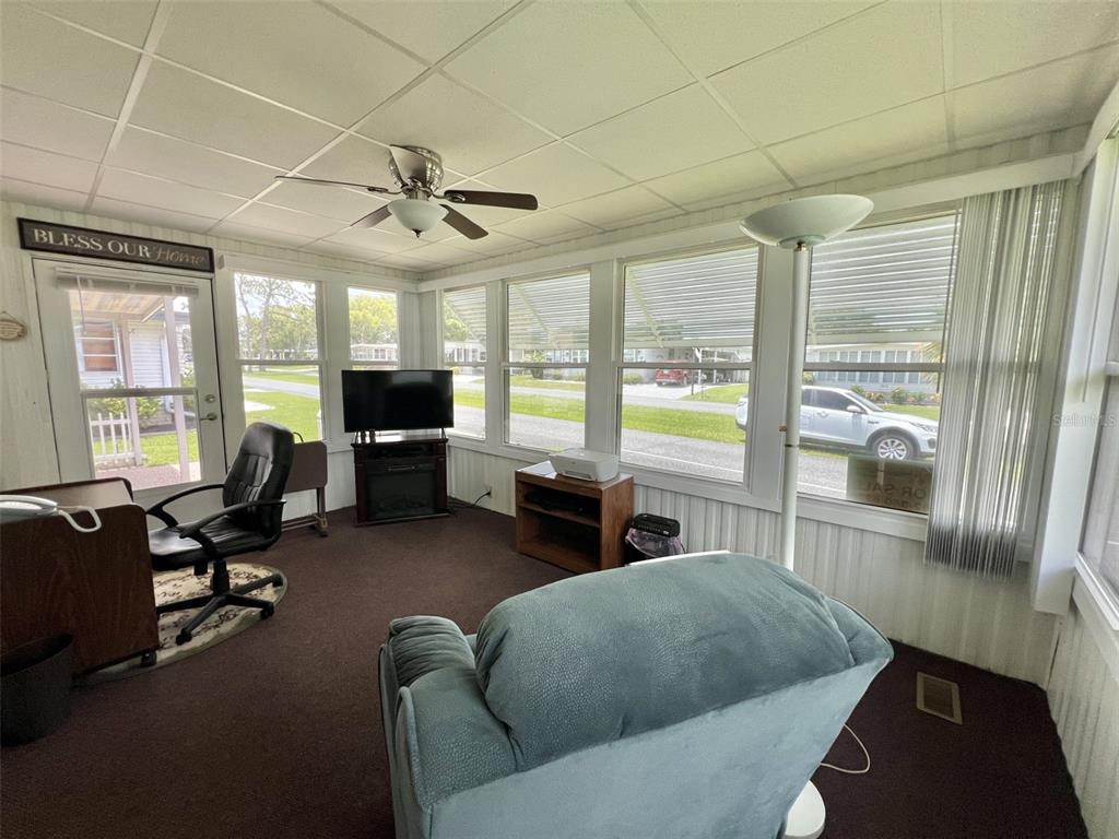 A sunroom with dark carpeting, a ceiling fan, and large windows looking out onto a street — 424 HAWTHORNE BOULEVARD, LEESBURG, FL