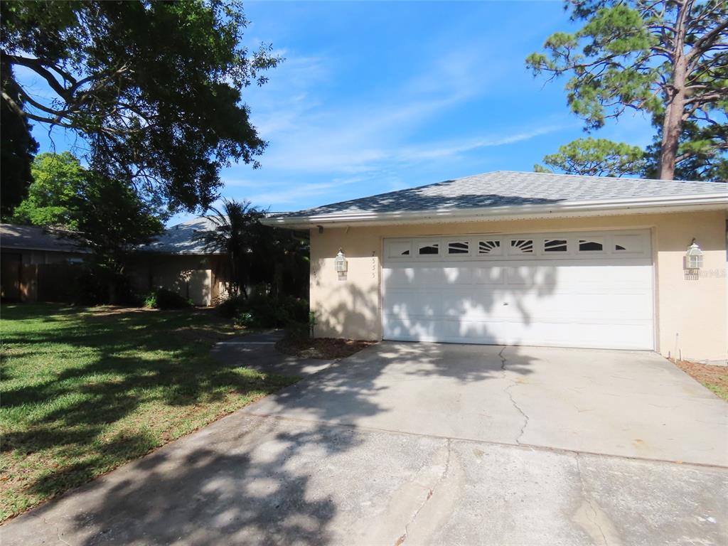 A single-story house with a white garage door, concrete driveway, and surrounding trees — 7555 PINE VALLEY LANE, SEMINOLE, FL