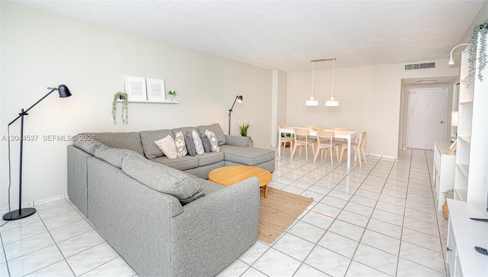 A living and dining area features a grey sectional sofa, tile flooring, and pendant lighting — 5601 Collins Ave # 1517, Miami Beach FL 33140, MIAMI BEACH, FL