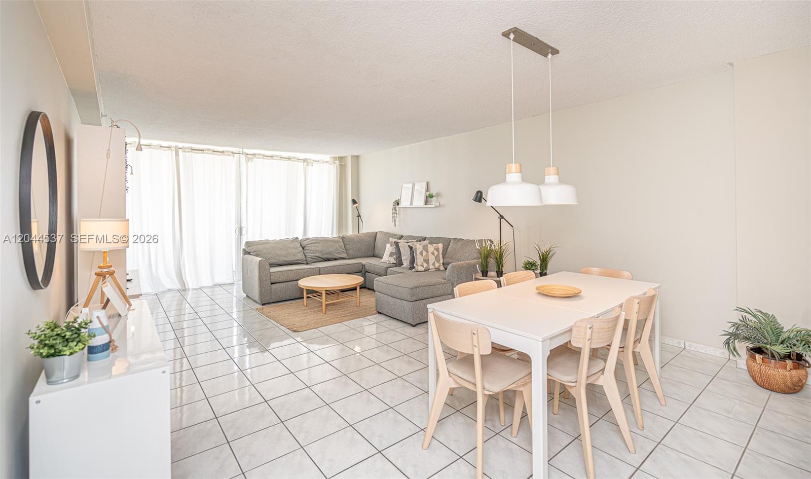 An open-concept living and dining area features white tile flooring, a gray sectional, and pendant lighting — 5601 Collins Ave # 1517, Miami Beach FL 33140, MIAMI BEACH, FL