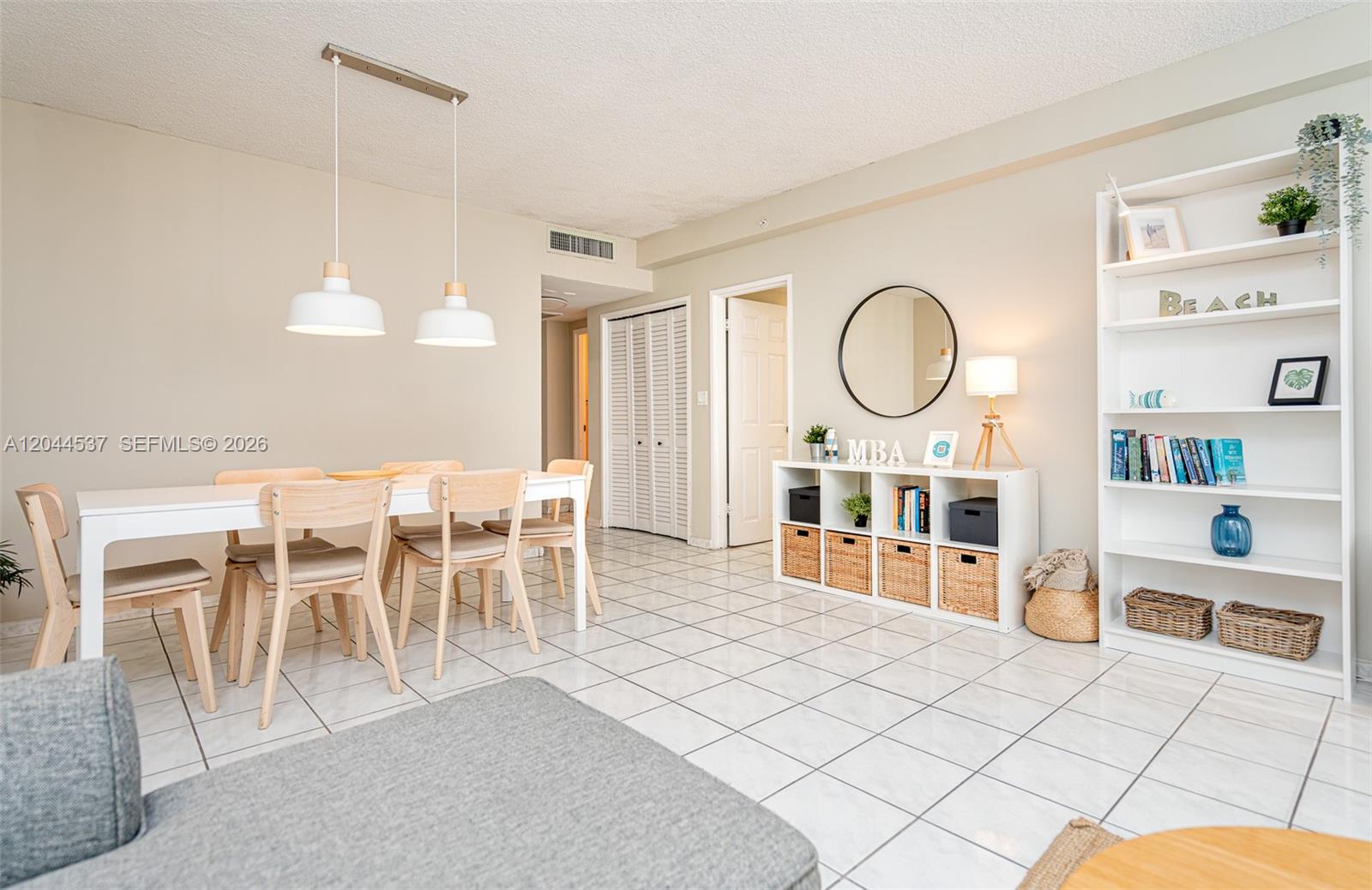 A dining area and living space feature white tile floors and a white bookshelf — 5601 Collins Ave # 1517, Miami Beach FL 33140, MIAMI BEACH, FL