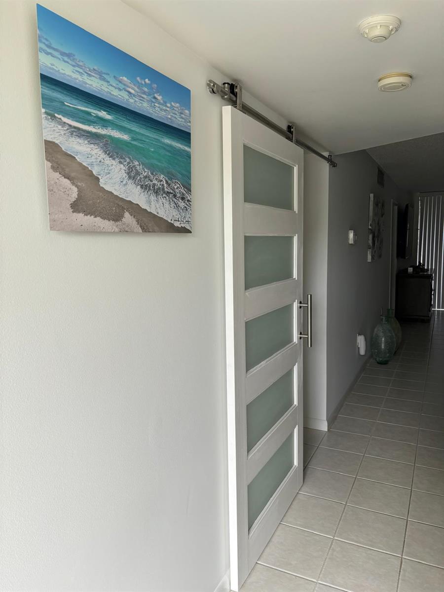 A white sliding barn door with frosted glass panels is installed in a tiled hallway — 9900 S Ocean Drive # 1, Jensen Beach FL 34957, JENSEN BEACH, FL