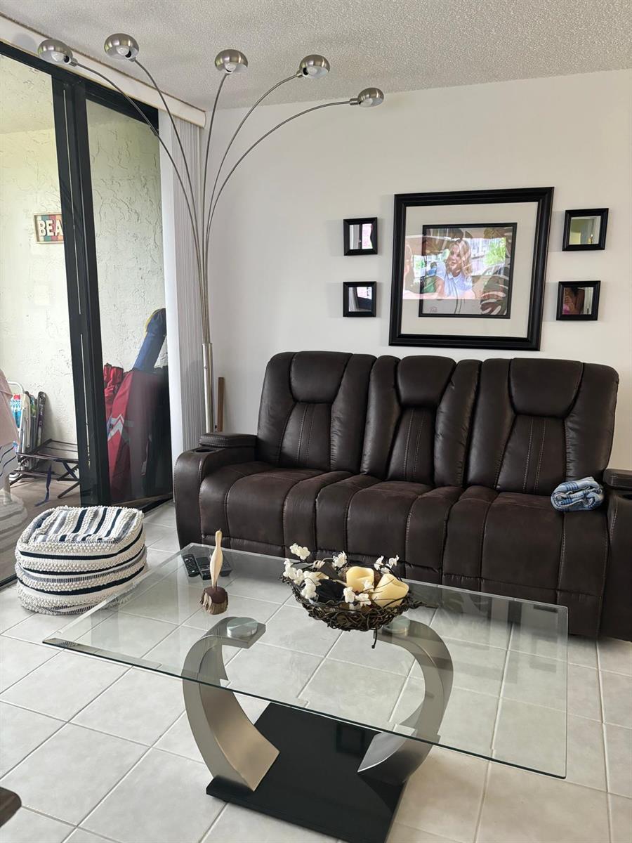 A living room features a brown leather sofa, a glass coffee table, and a floor lamp — 9900 S Ocean Drive # 1, Jensen Beach FL 34957, JENSEN BEACH, FL