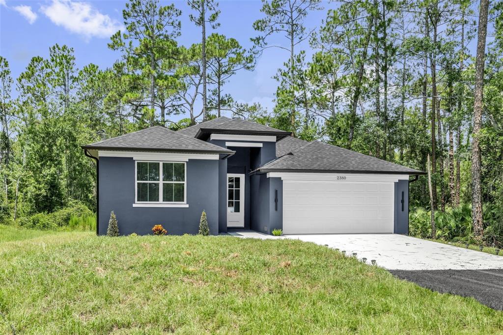 A single-story house with dark blue stucco siding, a white garage door, and surrounding trees — 2380 CENTRAL PARKWAY, DELAND, FL