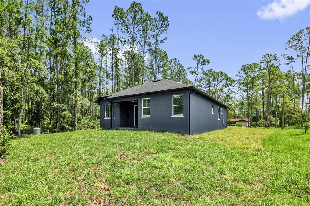 The rear exterior of a dark gray house features a covered patio and surrounding woods — 2380 CENTRAL PARKWAY, DELAND, FL