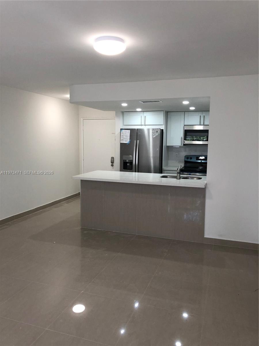 A kitchen with stainless steel appliances and a breakfast bar opens to a living area — 8883 Fontainebleau Blvd # A, Miami FL 33172, MIAMI, FL