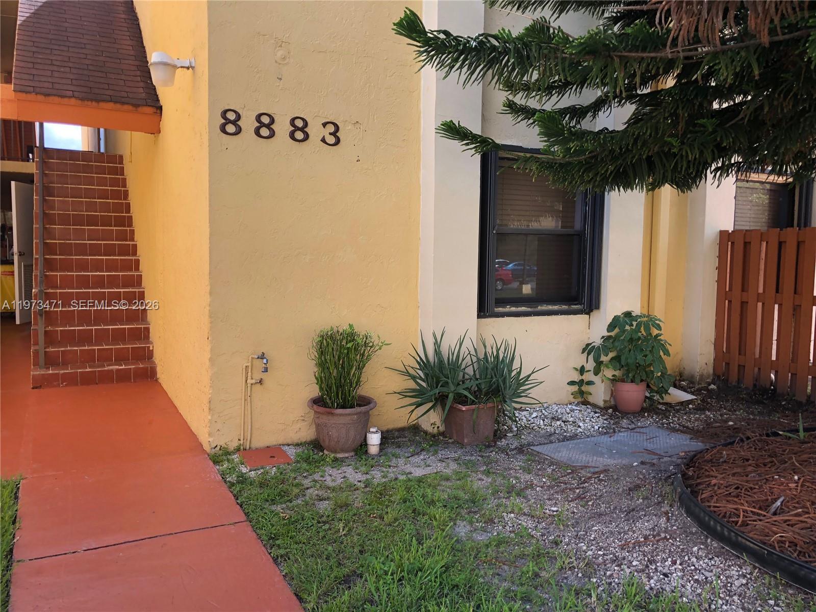 The exterior of a yellow building features a staircase, house number, and potted plants — 8883 Fontainebleau Blvd # A, Miami FL 33172, MIAMI, FL