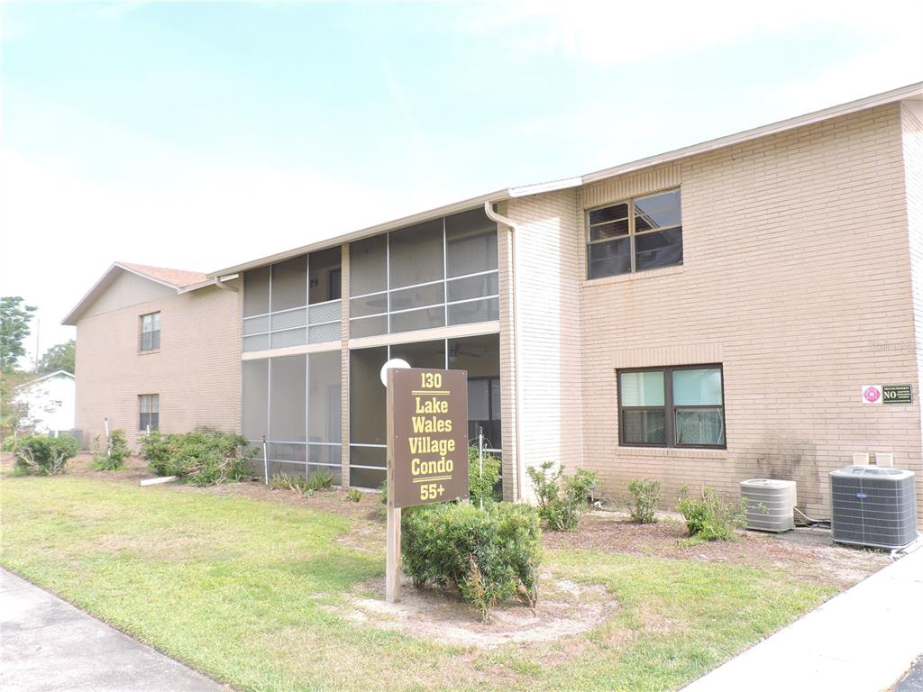 A two-story brick apartment building features screened-in balconies and a sign for a 55+ community — 130 E JOHNSON AVENUE UNIT 102, LAKE WALES, FL