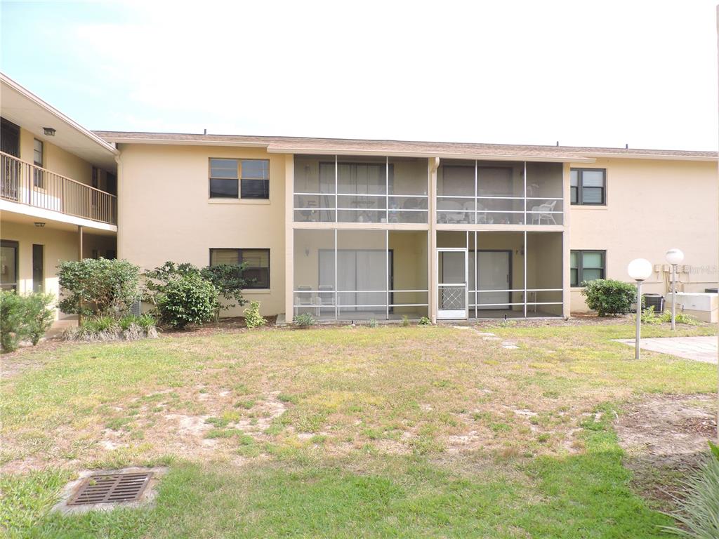 The exterior view shows a two-story apartment building with screened-in balconies and a lawn — 130 E JOHNSON AVENUE UNIT 102, LAKE WALES, FL