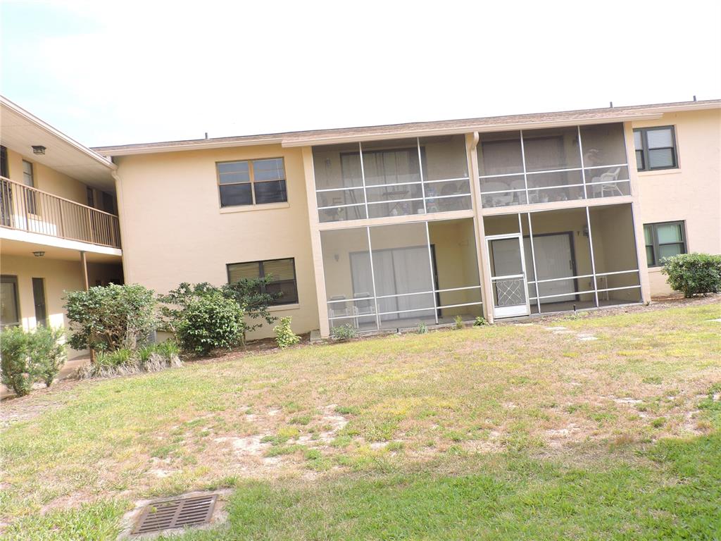 A two-story apartment building features tan stucco walls and screened-in porches on the ground level — 130 E JOHNSON AVENUE UNIT 102, LAKE WALES, FL