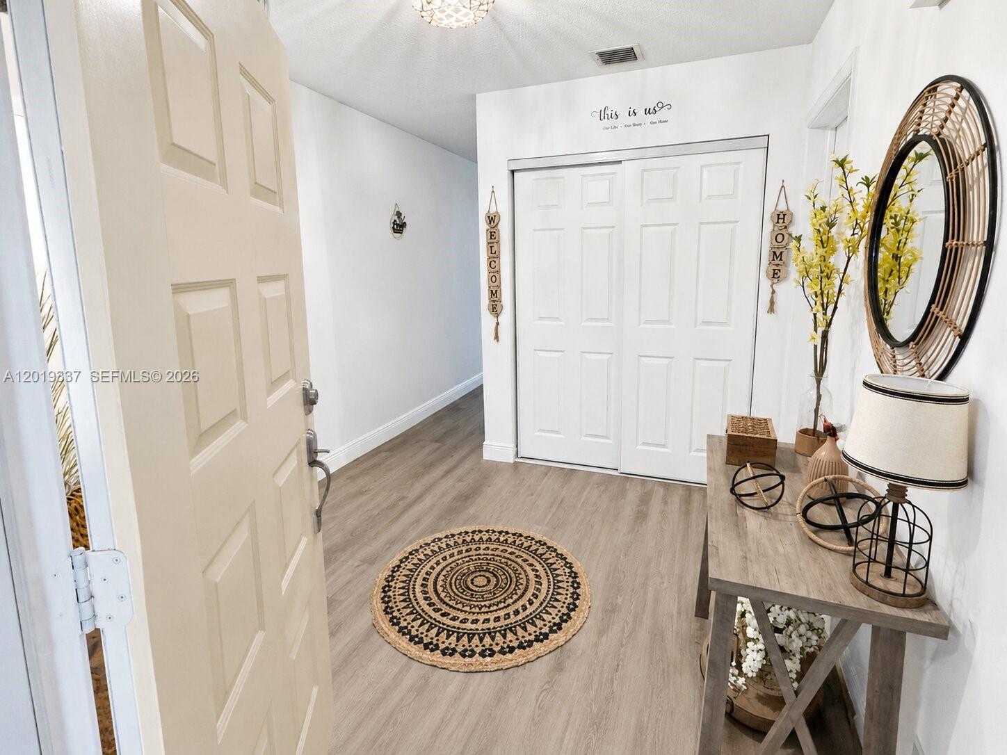 An entryway features light wood flooring, a round rug, a console table, and closet doors — 11913 Donlin Dr, Wellington FL 33414, WELLINGTON, FL
