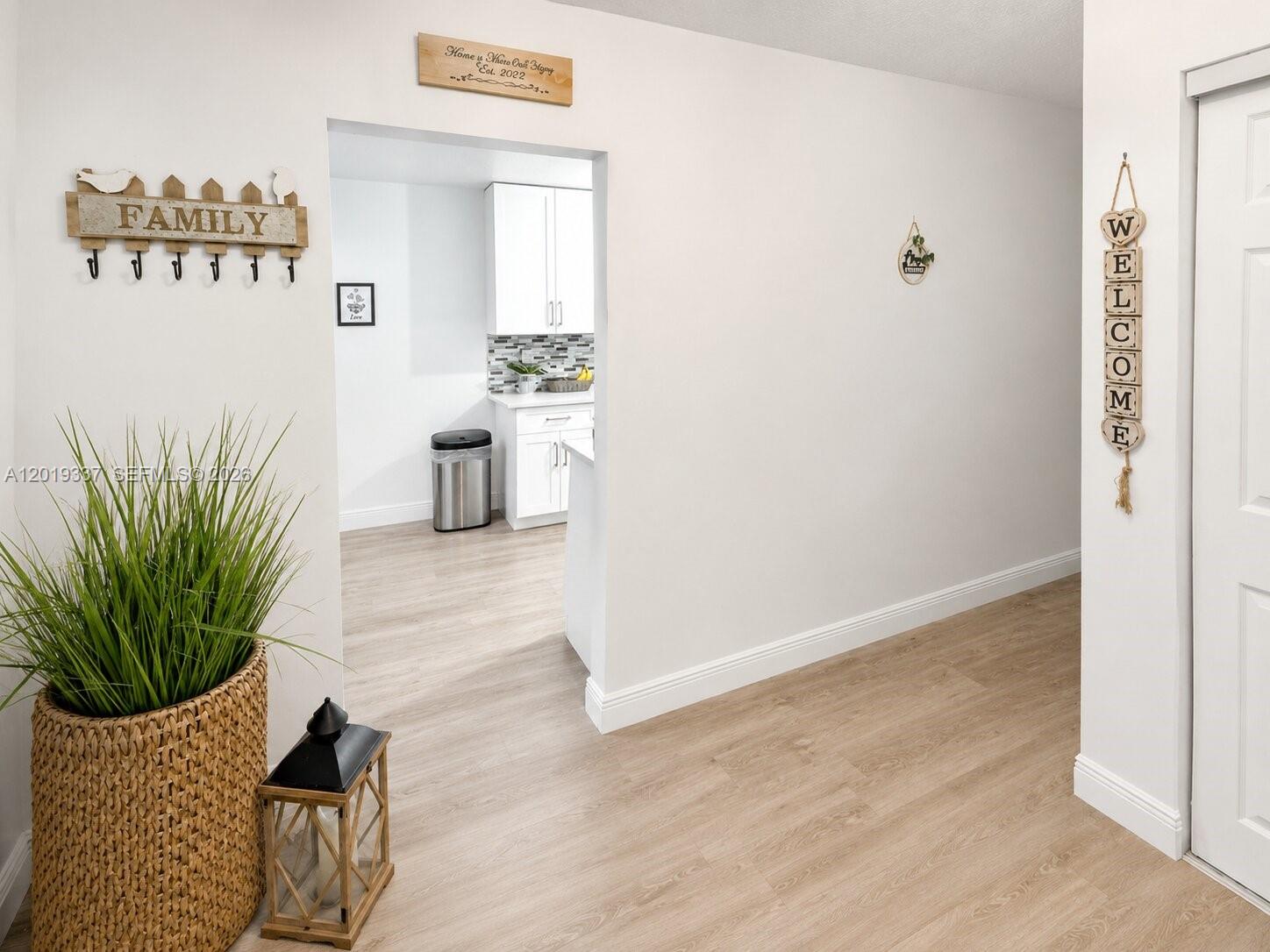 A hallway with light wood-look flooring leads into a kitchen with white cabinets — 11913 Donlin Dr, Wellington FL 33414, WELLINGTON, FL