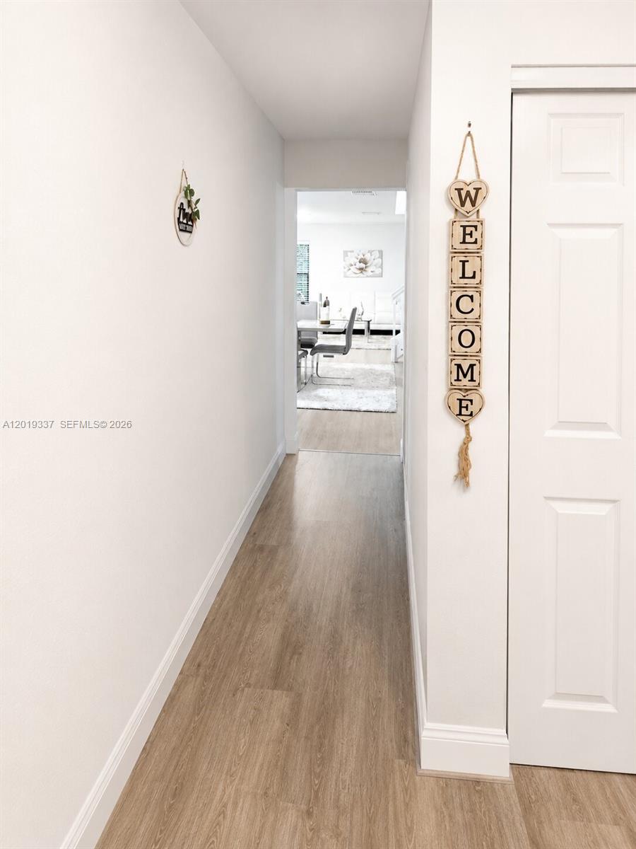 A hallway with light wood-look flooring leads to a dining area in the background — 11913 Donlin Dr, Wellington FL 33414, WELLINGTON, FL