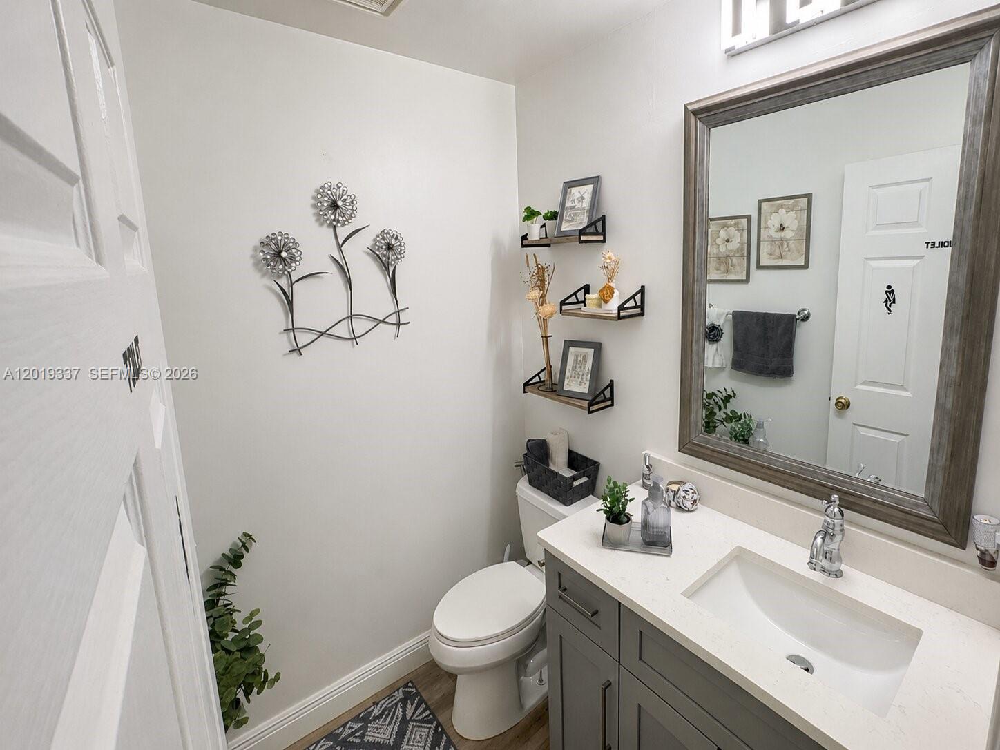 A small bathroom features a gray vanity, a toilet, and wall-mounted shelves with decor — 11913 Donlin Dr, Wellington FL 33414, WELLINGTON, FL