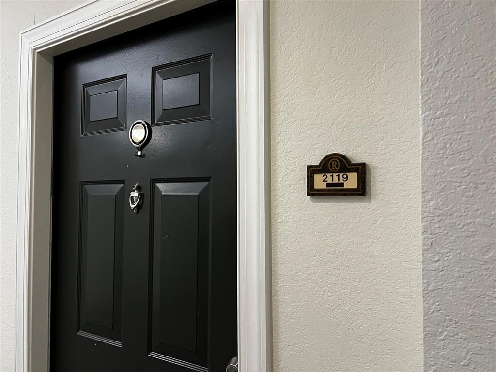 A black front door with a silver peephole and knocker features a unit number sign — 5550 E MICHIGAN STREET UNIT 2119, ORLANDO, FL