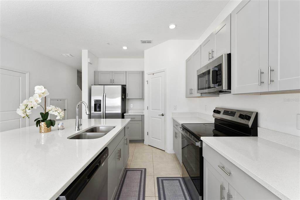 A modern kitchen features gray cabinets, stainless steel appliances, and a large white quartz island — 5131 QUAKERS PLACE, ST CLOUD, FL