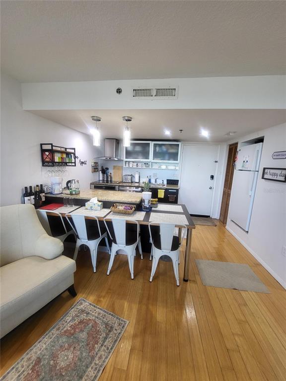 A kitchen with a breakfast bar, white chairs, and hardwood floors opens to a living area — 701 S MADISON AVENUE UNIT 414, CLEARWATER, FL