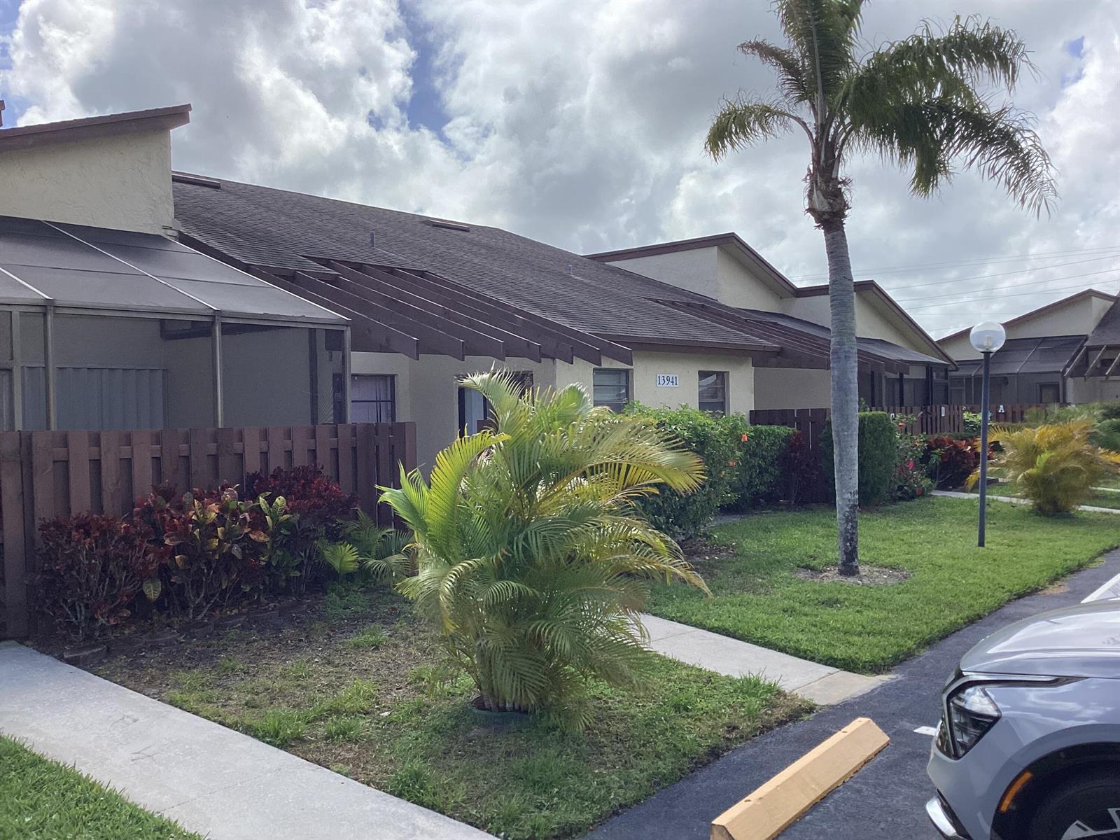 A single-story residential building with a brown roof, a palm tree, and a small lawn — 13941 Nesting Way # C, Delray Beach FL 33484, DELRAY BEACH, FL