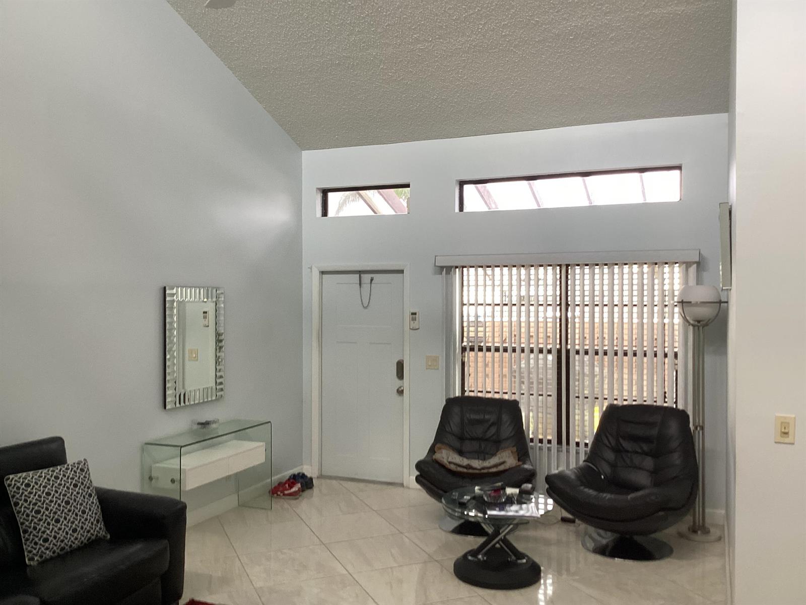 A living room features vaulted ceilings, tile flooring, a glass console table, and two leather chairs — 13941 Nesting Way # C, Delray Beach FL 33484, DELRAY BEACH, FL