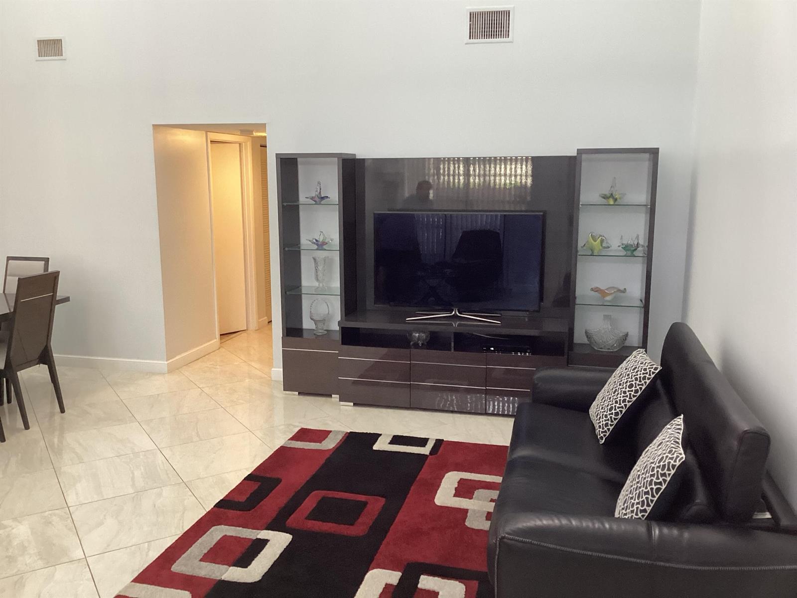 A living room features a dark entertainment center, a black leather sofa, and a patterned rug — 13941 Nesting Way # C, Delray Beach FL 33484, DELRAY BEACH, FL