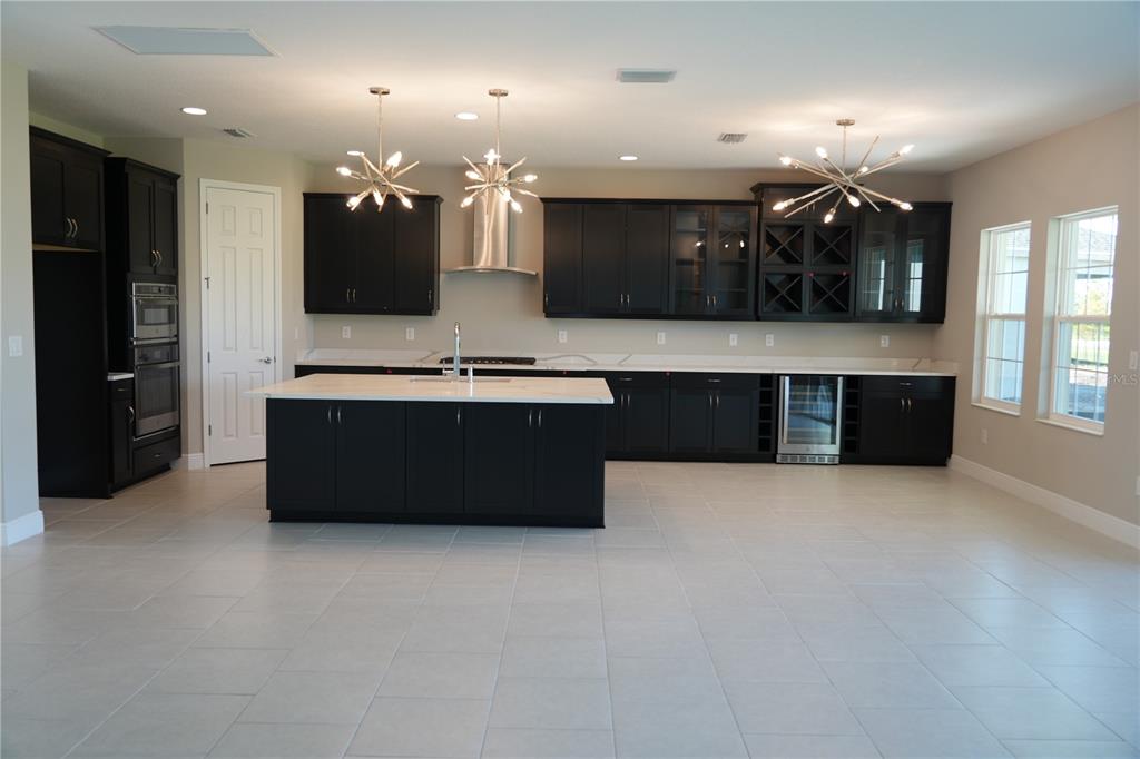 A modern kitchen features dark cabinetry, a large white island, and three sputnik-style light fixtures — 5450 WAYFARER AVENUE, APOLLO BEACH, FL