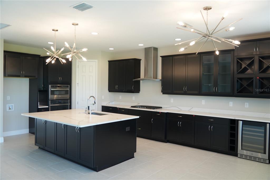 A modern kitchen features dark cabinets, a large white island, and two sputnik-style light fixtures — 5450 WAYFARER AVENUE, APOLLO BEACH, FL