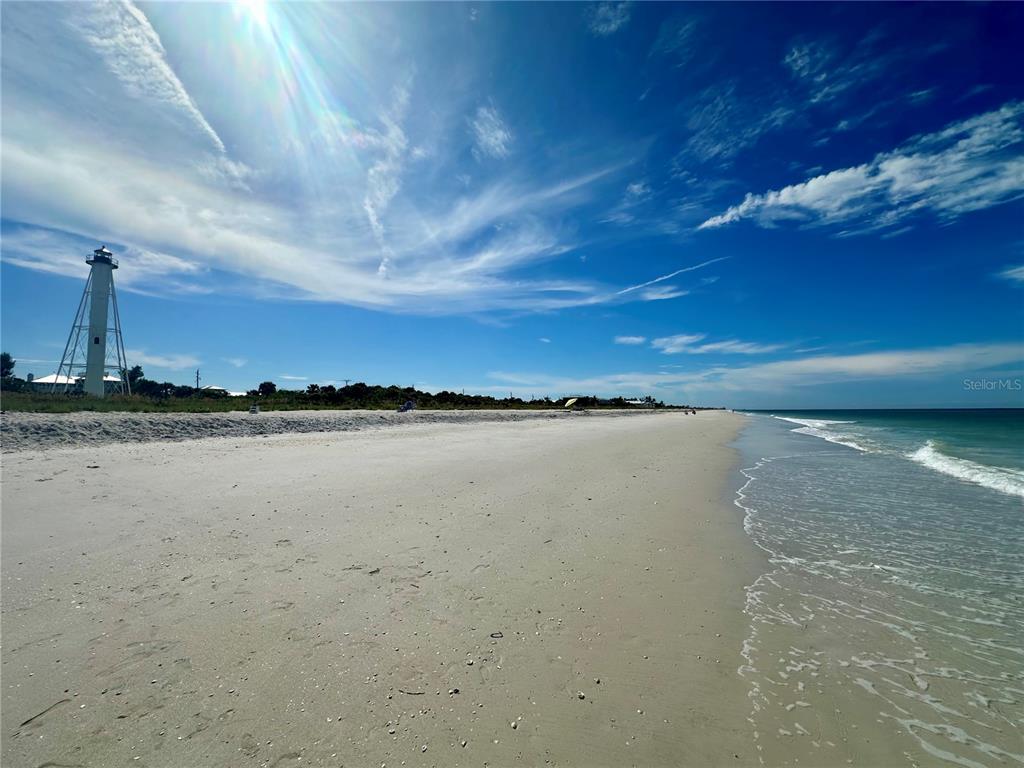A sandy beach stretches toward a tall lighthouse under a bright blue sky — 9487 ROSEBUD CIRCLE, PORT CHARLOTTE, FL
